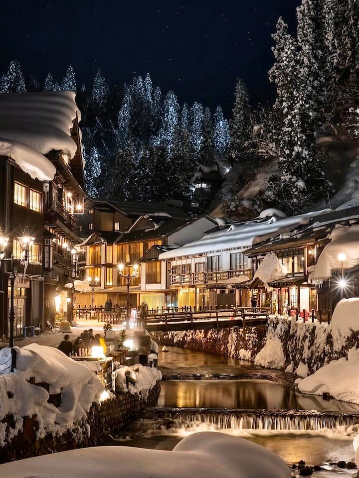 Nostalgic street in Ginzan Onsen illuminated by kerosene lamps with traditional wooden buildings and a snowy winter landscape